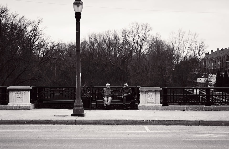 Members of Girl Stand Still sitting on a bench on a bridge in Old Town Lansing, Michigan